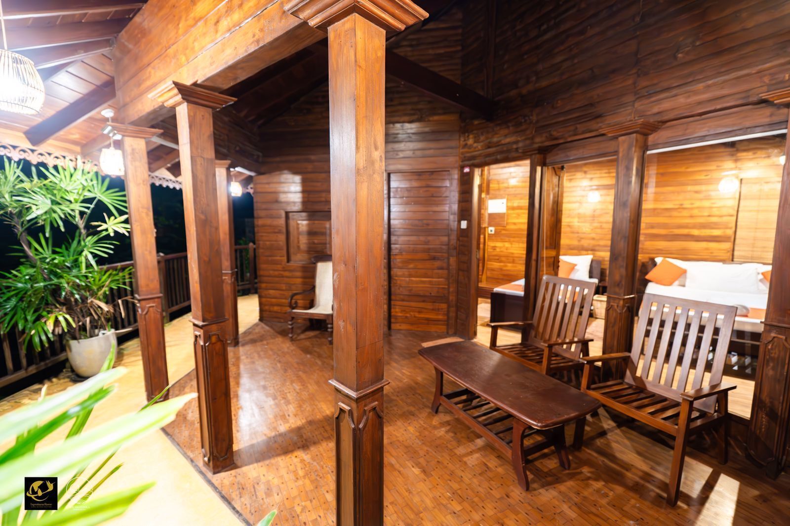 Interior de una cabaña de madera con comedor, cama y planta en maceta.