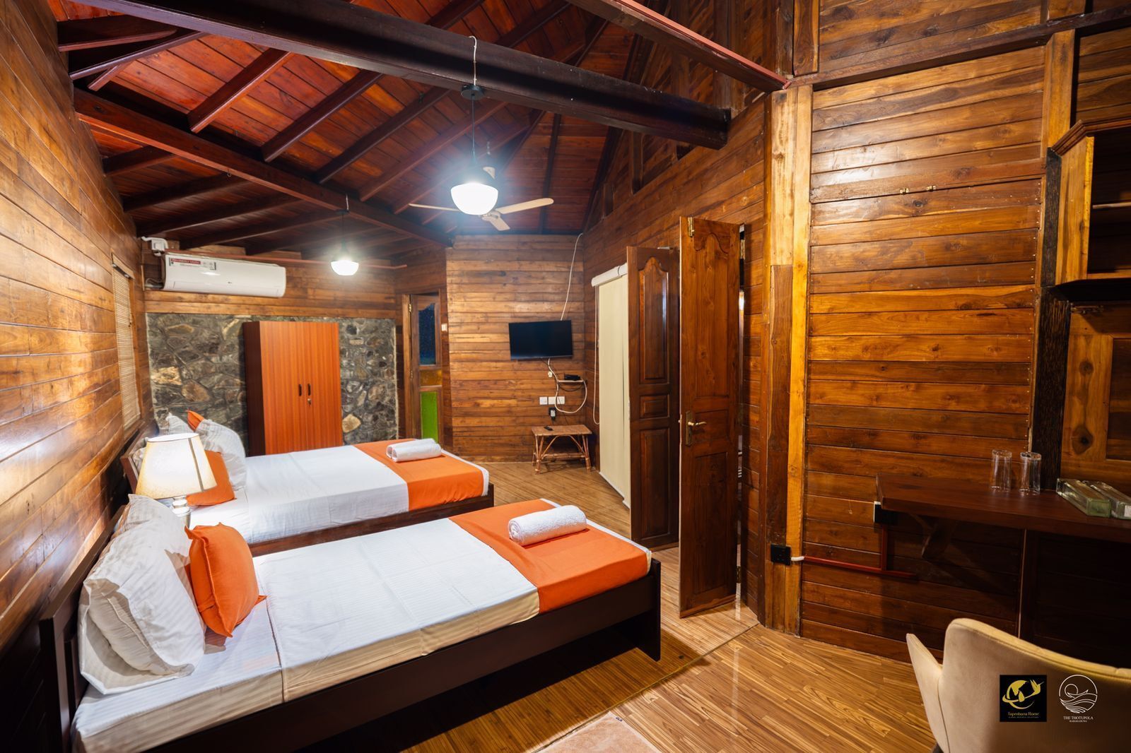A wooden cabin with two beds, a television, and a desk.