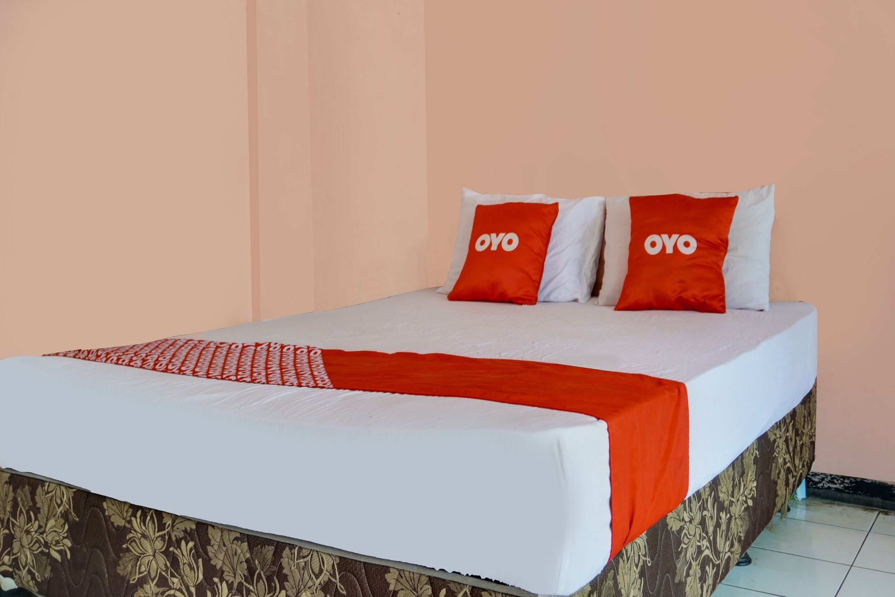 Una cama con colchón blanco, dos almohadas con la marca 'OYO' y una manta roja.