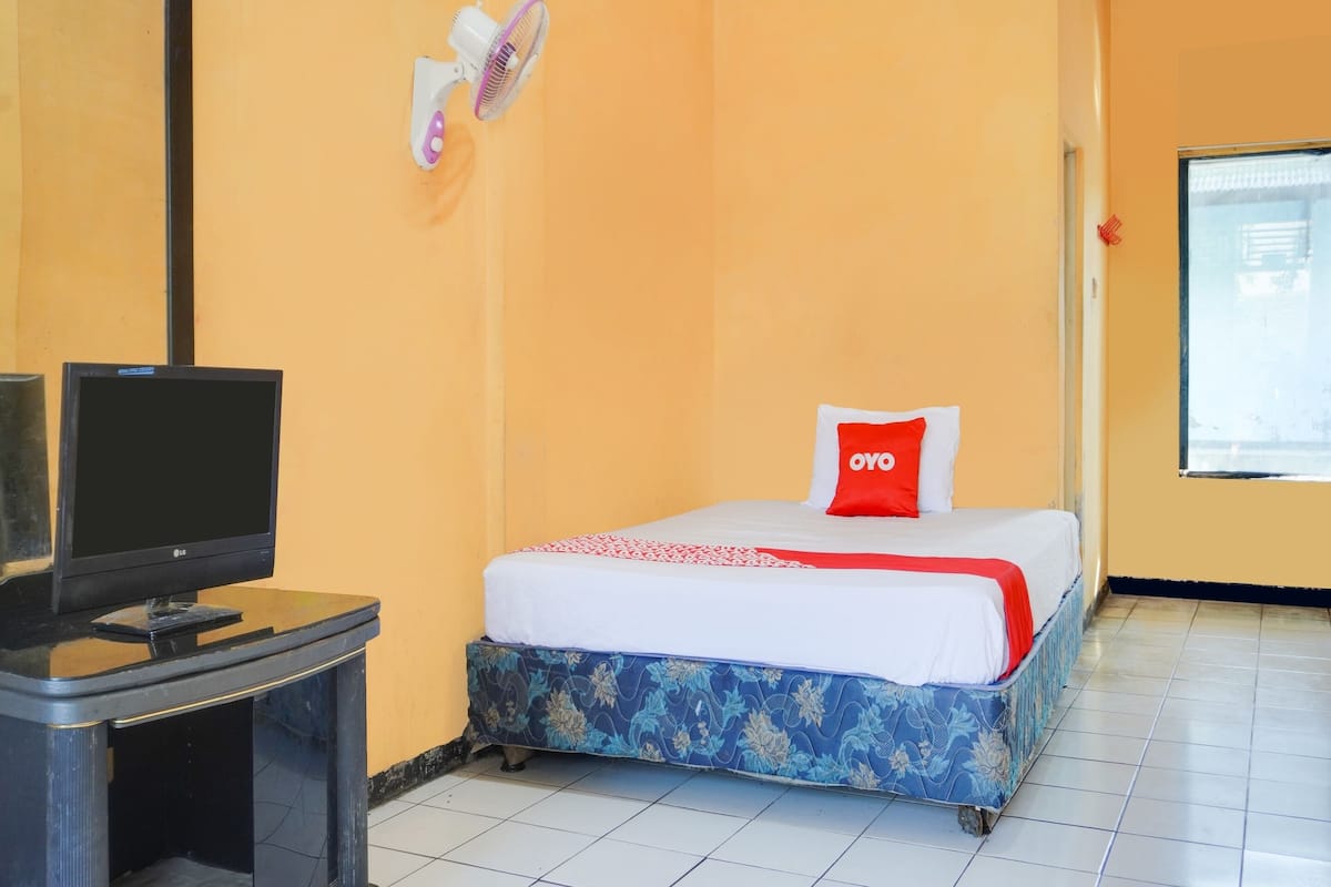 Une chambre avec un lit, un téléviseur posé sur un meuble et une fenêtre.