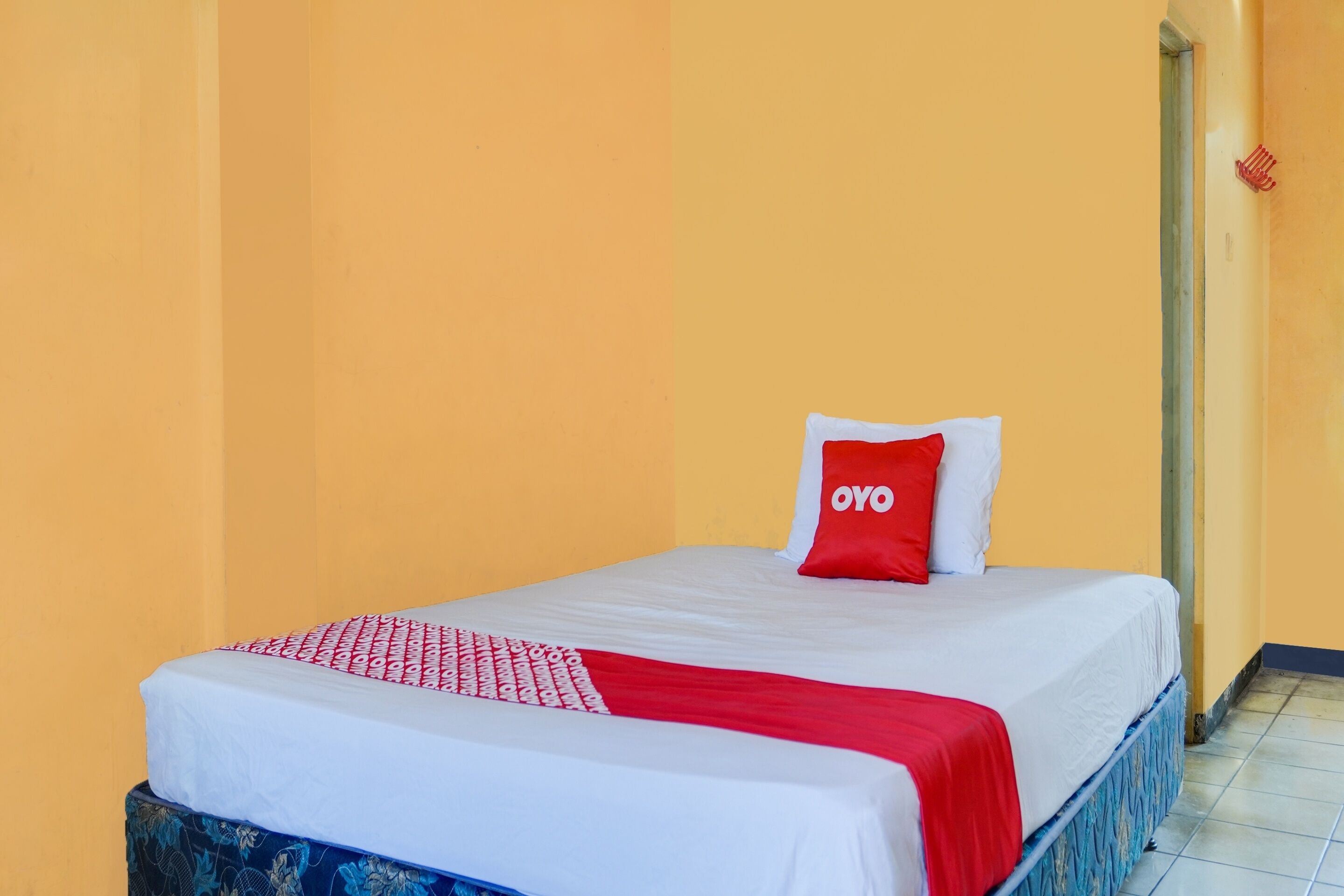 Un lit simple avec une couvre-lit blanche et rouge, un oreiller rouge orné du texte « OYO » et un oreiller bleu à motifs.
