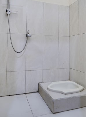 A bathroom with white tiled walls, a shower with a flexible hose, and a white pedestal sink.