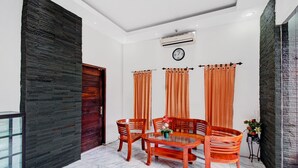 A dining area with a round table and four wooden chairs, a clock on the wall, and a window with curtains.