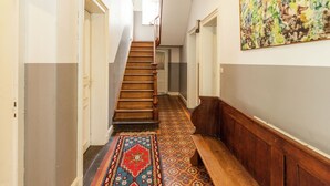 Ein Flur mit einer Holztreppe, einem gemusterten Teppich und einem großen abstrakten Gemälde an der Wand.