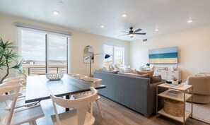 Un salon moderne comprenant un coin repas, un canapé gris et un ventilateur de plafond.