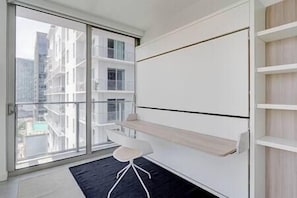 A modern room with a sliding glass door leading to a balcony, a white chair, and a built-in shelf unit. - Luxury apt. in the bay front park (Miami)