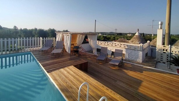 Un área de piscina en la azotea con cubierta de madera, sillones de descanso y un espacio de estar techado.