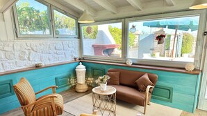 Una habitación acogedora con un sofá marrón, una silla a rayas y un sillón amarillo. Un farol blanco y una pequeña mesa con flores están en el suelo.
