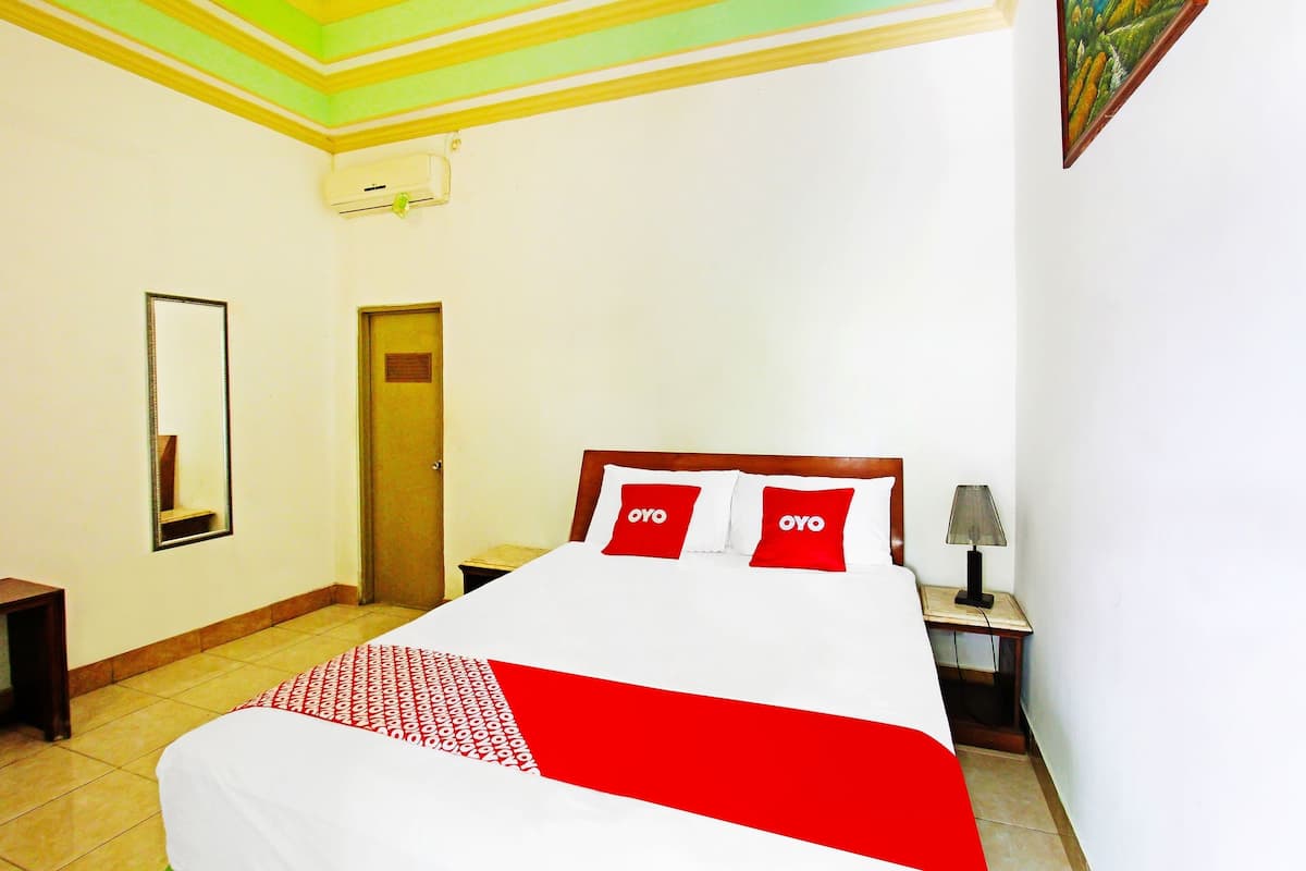 A hotel room with a bed, a nightstand, a lamp, a mirror, and a door.