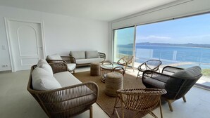 Una sala de estar moderna con muebles de mimbre, una mesa de vidrio y un amplio ventanal con vistas al mar.