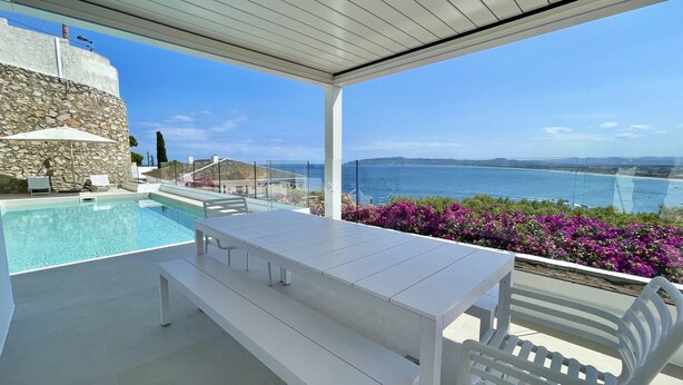 Zona de piscina con mesa y sillas, con vistas panorámicas al mar y a las montañas.