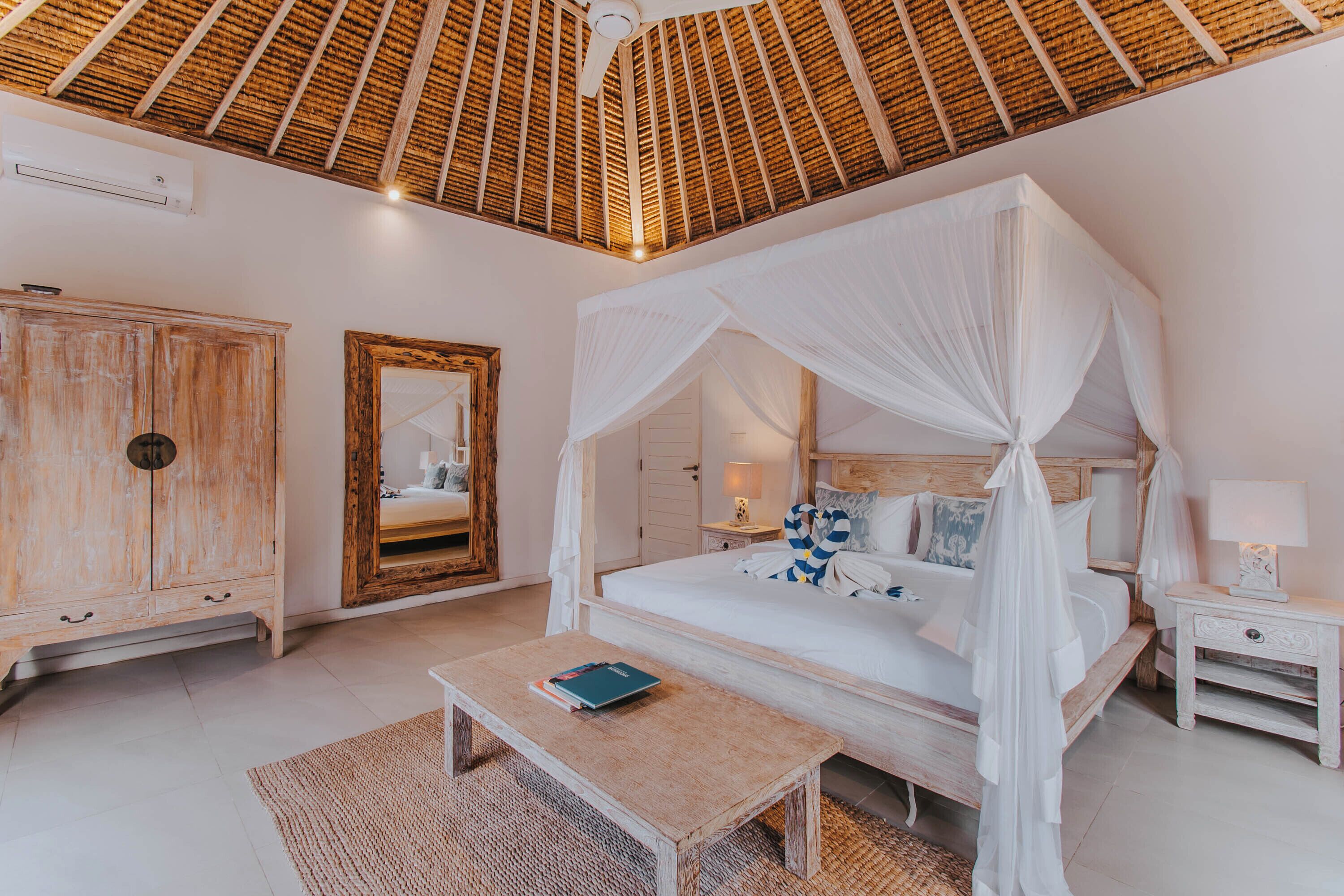 Een slaapkamer met een hemelbed, een houten garderobe, een spiegel en een nachtkastje met een lamp.