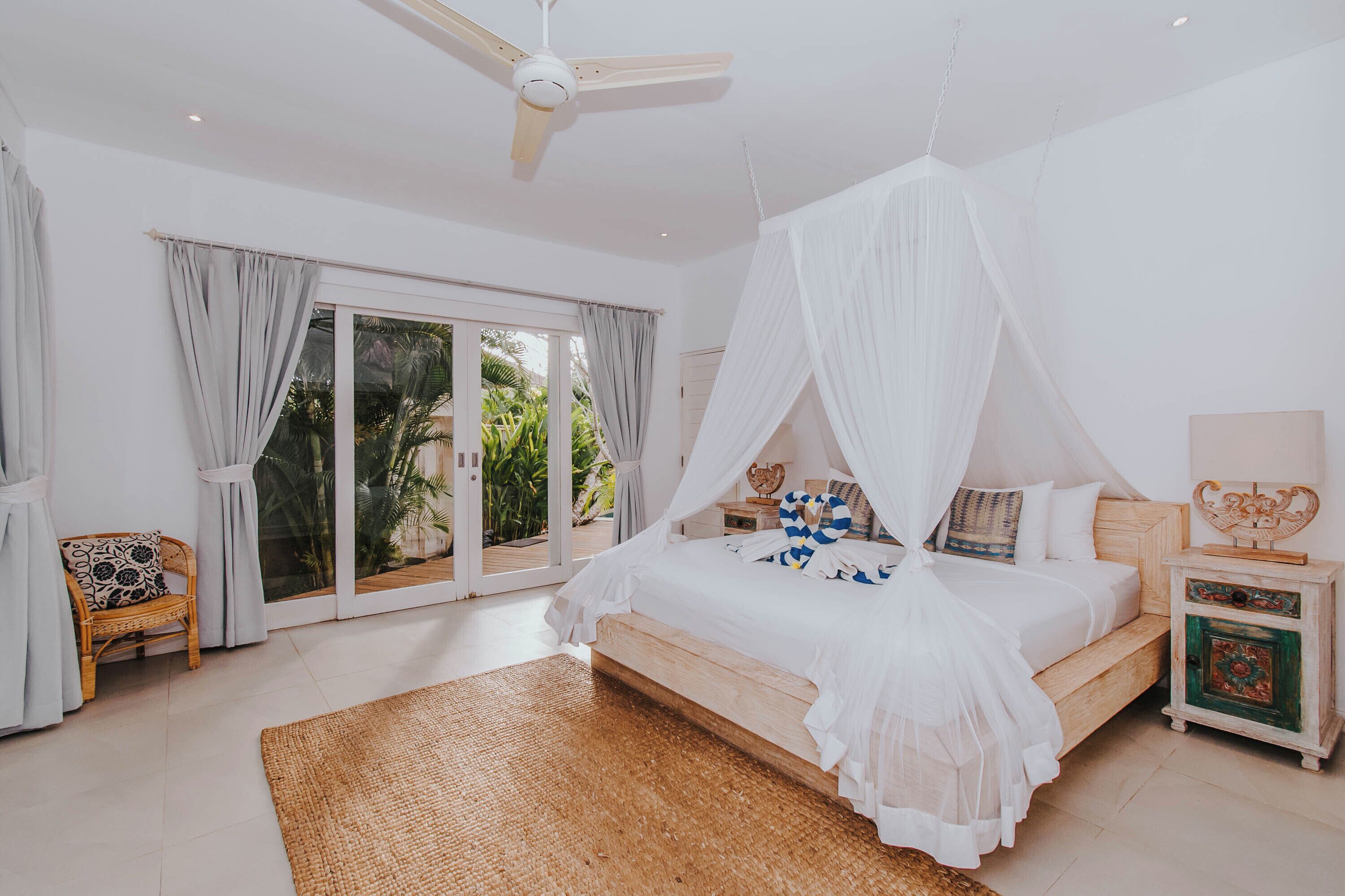 Un dormitorio con una cama, una mesita de noche, una silla y un ventanal con cortinas.
