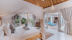 Ein geräumiges Schlafzimmer mit einem großen Bett, einem Baldachin und Blick auf einen Poolbereich.