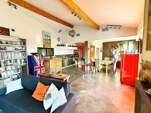 Uma sala de estar ampla com sofá, estante de livros e um espaço de refeições com cadeiras e mesa.