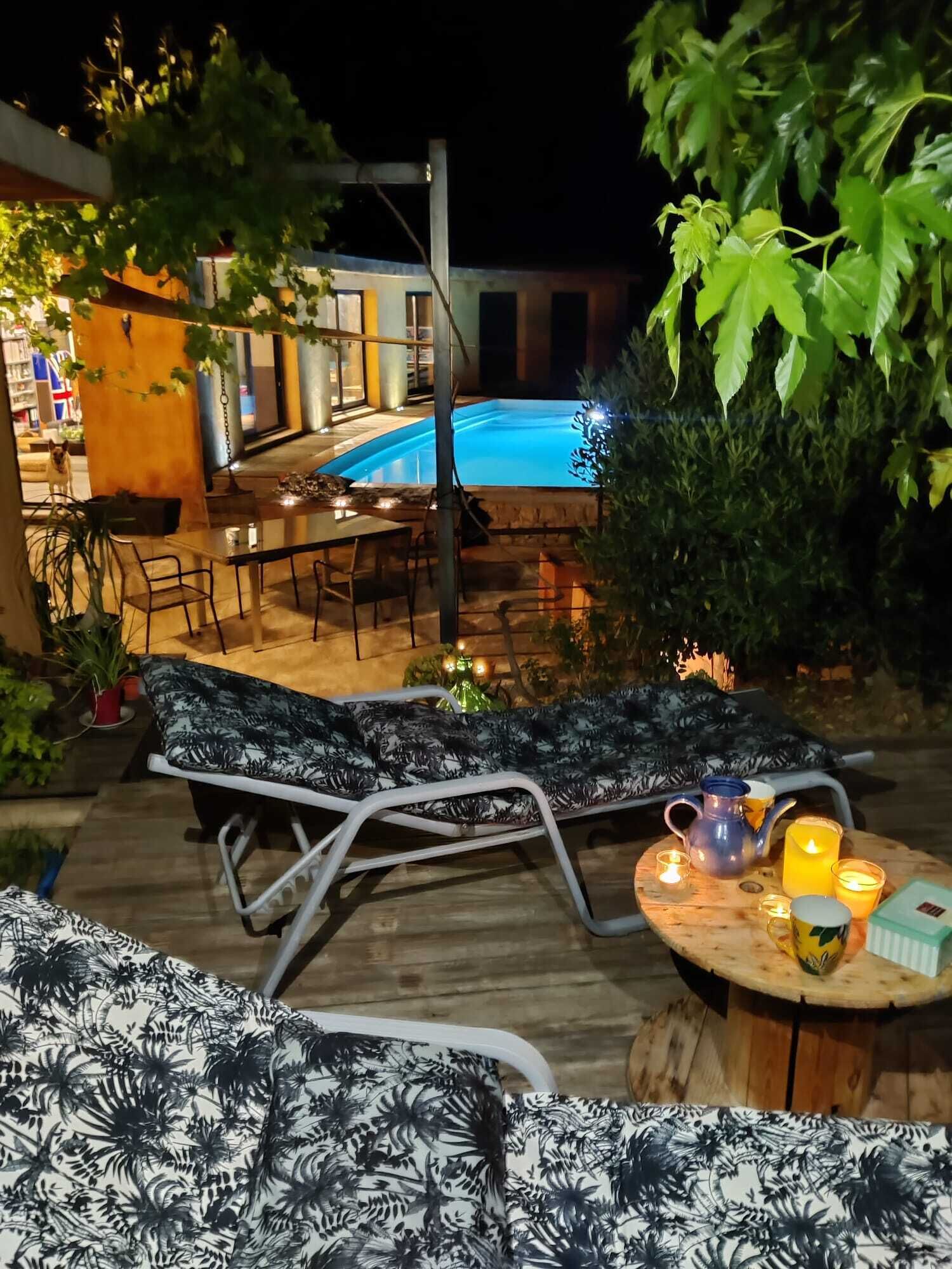 A poolside area with a lounge chair, a table with candles, and a view of a swimming pool.
