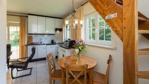 Eine Küche mit weißen Schränken, einem Holzespeisetisch mit vier Stühlen, einer Kaffeemaschine und einem Fenster mit Vorhängen.