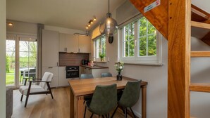 Eine moderne Küche mit Holzausstattung, einem Esstisch mit Stühlen und einem großen Fenster mit Blick ins Grüne.