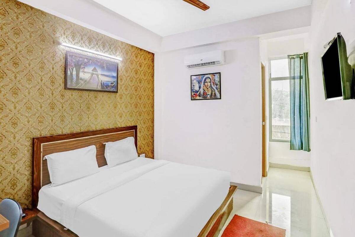 A hotel room with a bed, a ceiling fan, a wall-mounted air conditioner, and a window with curtains.