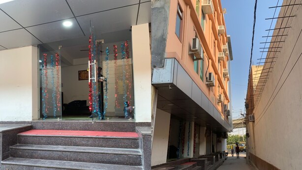 A building entrance with steps leading up to a door, a narrow alleyway beside it, and a multi-story building in the background. - Hotel Noida Continental  (Noida)