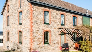 A stone building with a sloped roof, multiple windows, and a small patio area with outdoor seating. - Pretty Farmhouse in Houffalize with Courtyard (Houffalize)