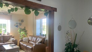 A living room with a brown leather sofa, a wooden coffee table, and a rug. There are potted plants and a hanging plant with heart-shaped leaves. - Pretty Farmhouse in Houffalize with Courtyard (Houffalize)