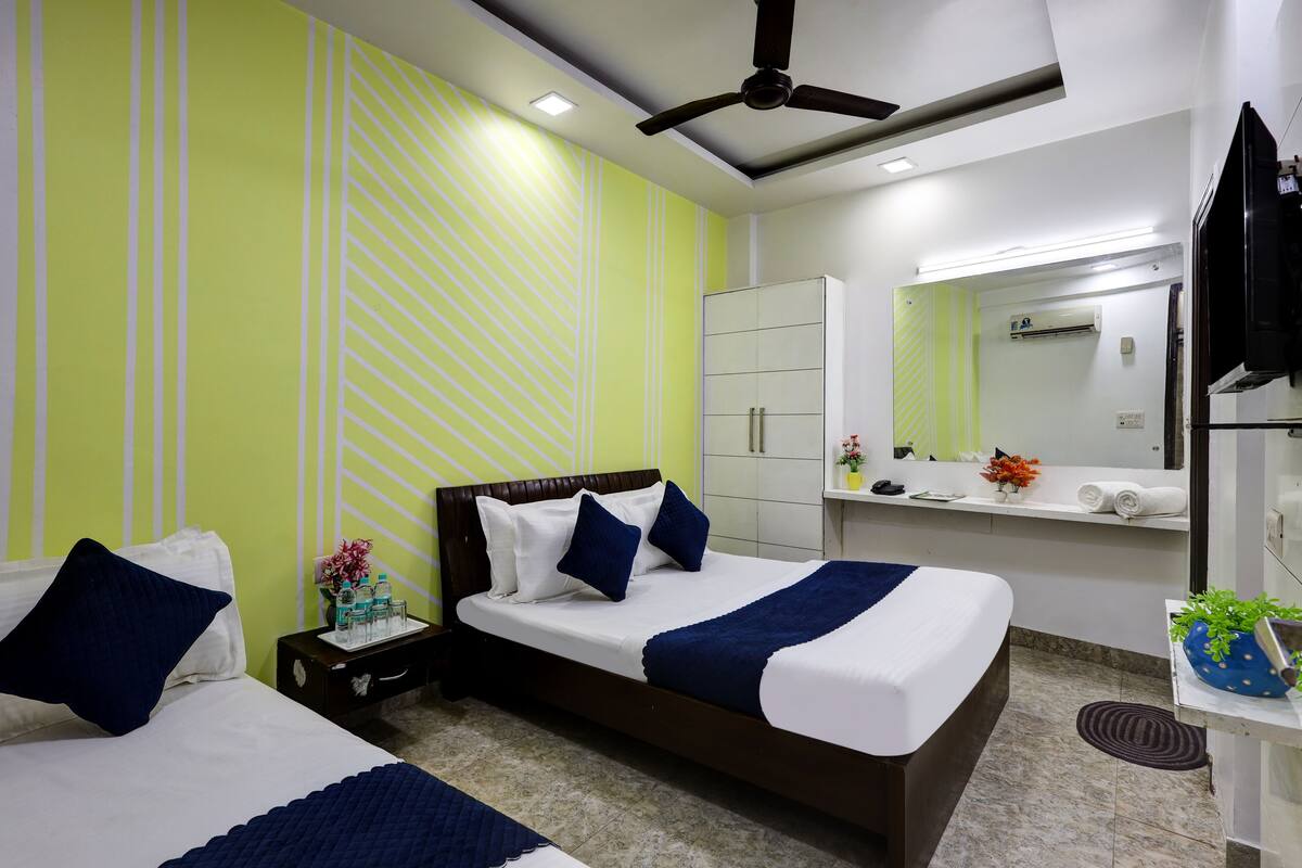 A hotel room with two beds, a ceiling fan, a large mirror, and a small bathroom area.