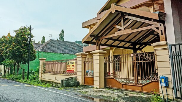 A residential building with a covered porch, a gated entrance, and a green fence in the background.