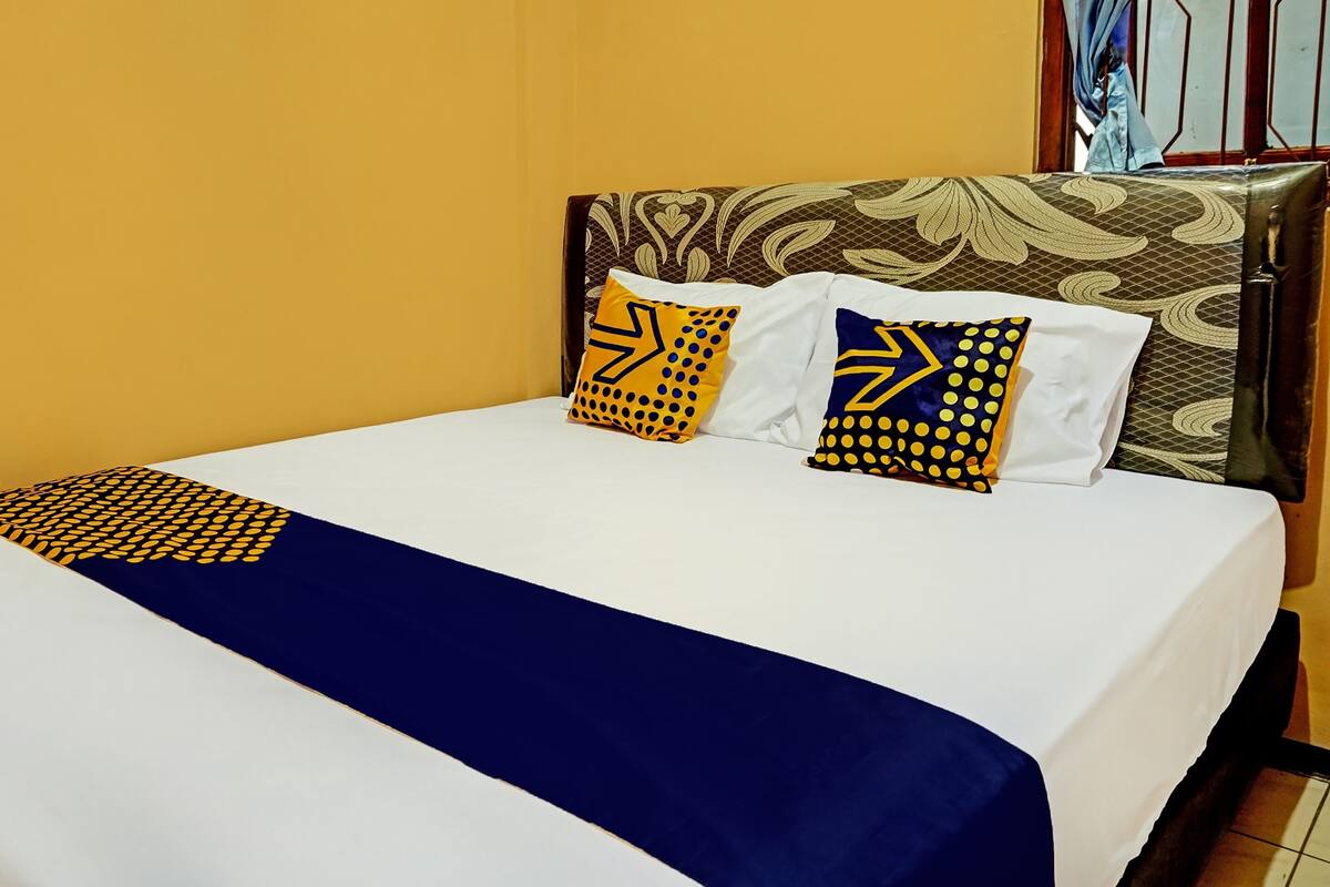 Ein Bett mit weißblauer Bettdecke, zwei Kissen mit gelbblauen Mustern und ein braunes Kopfstück mit floralem Dekor.