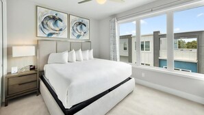 A modern bedroom with a large bed, a nightstand, a ceiling fan, and a view of a building through large windows.