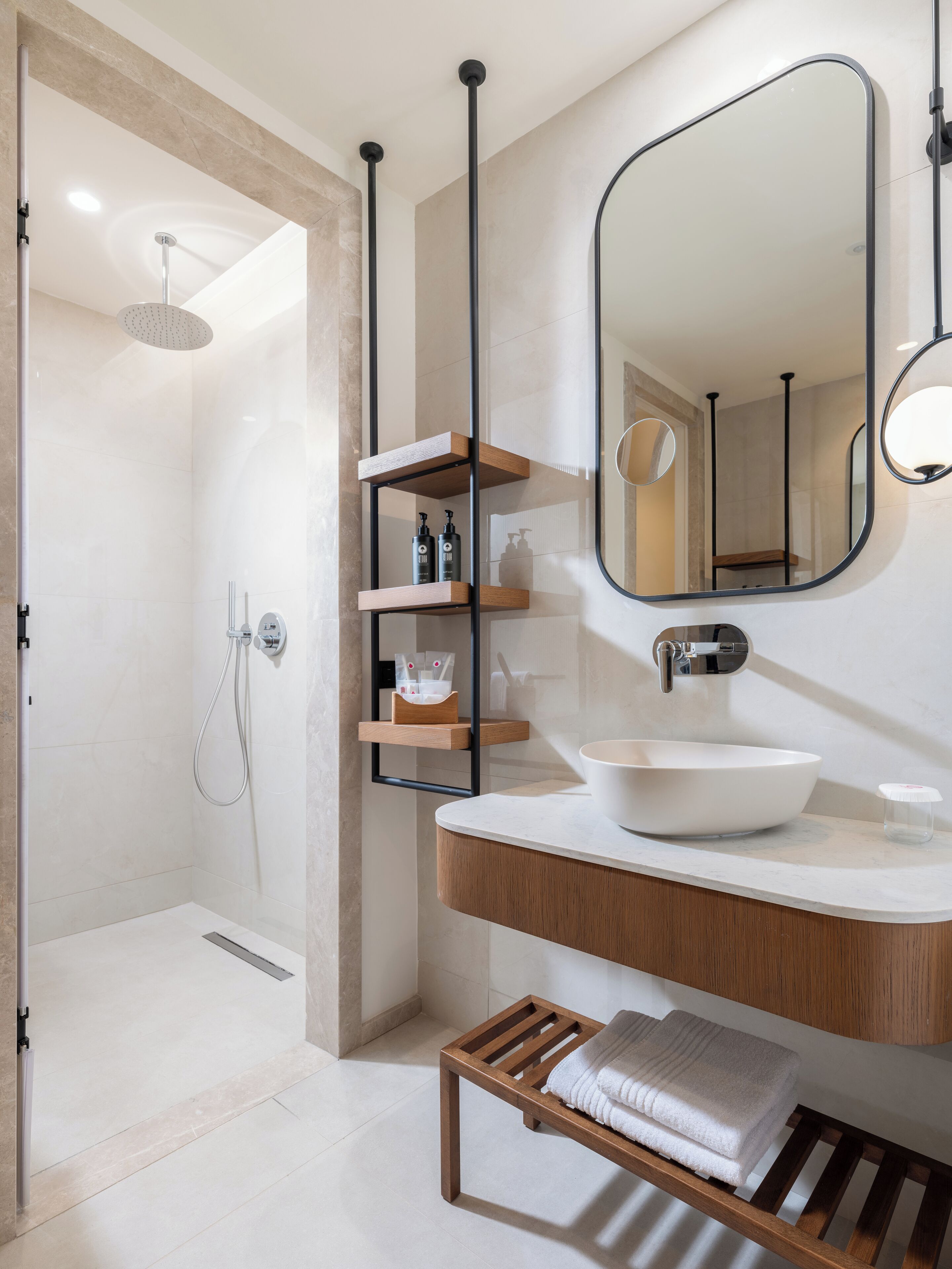 A modern bathroom with a large white sink, a wooden shelf with toiletries, a mirror, and a shower area.