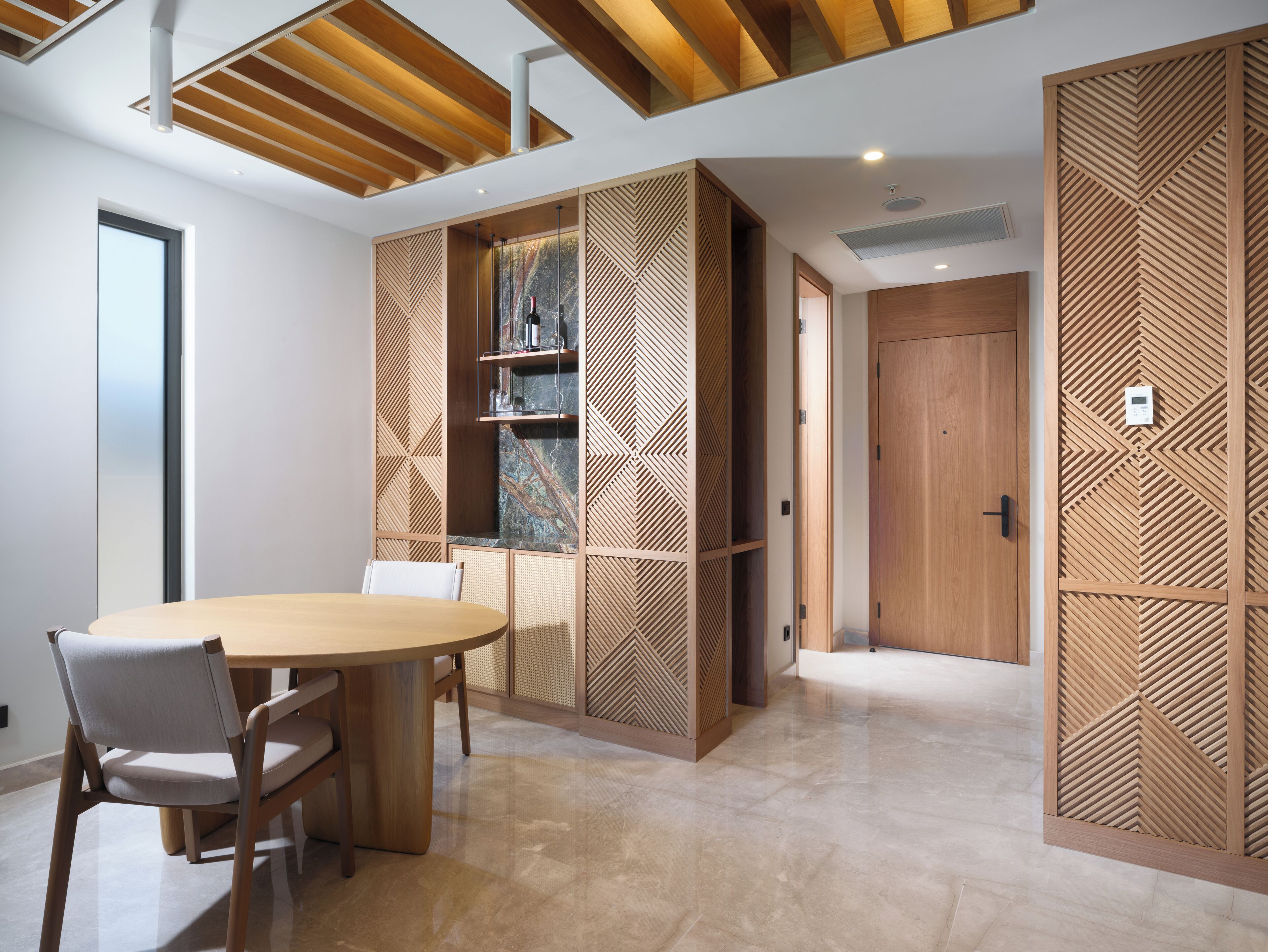 Una sala de conferencias moderna con una mesa y sillas de madera, un ventanal grande y un panel decorativo de madera con motivos geométricos.