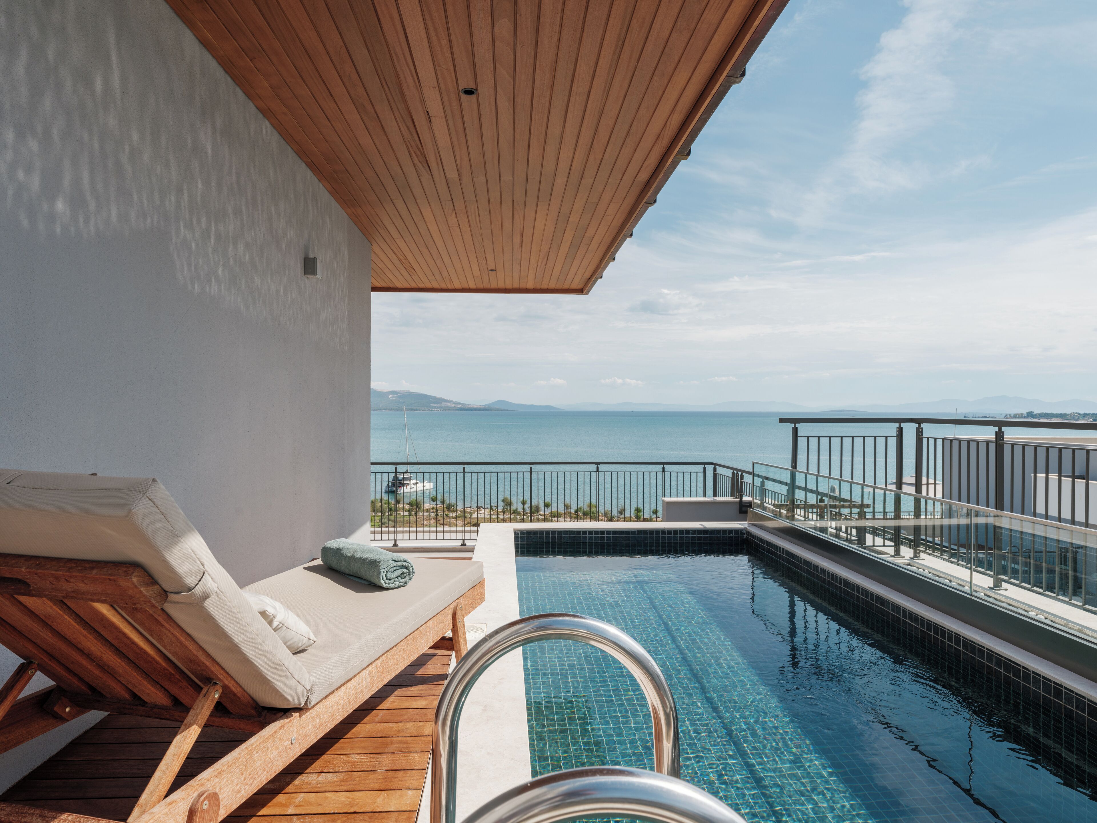 Un área de piscina con terraza de madera, una silla de descanso y vista al mar.