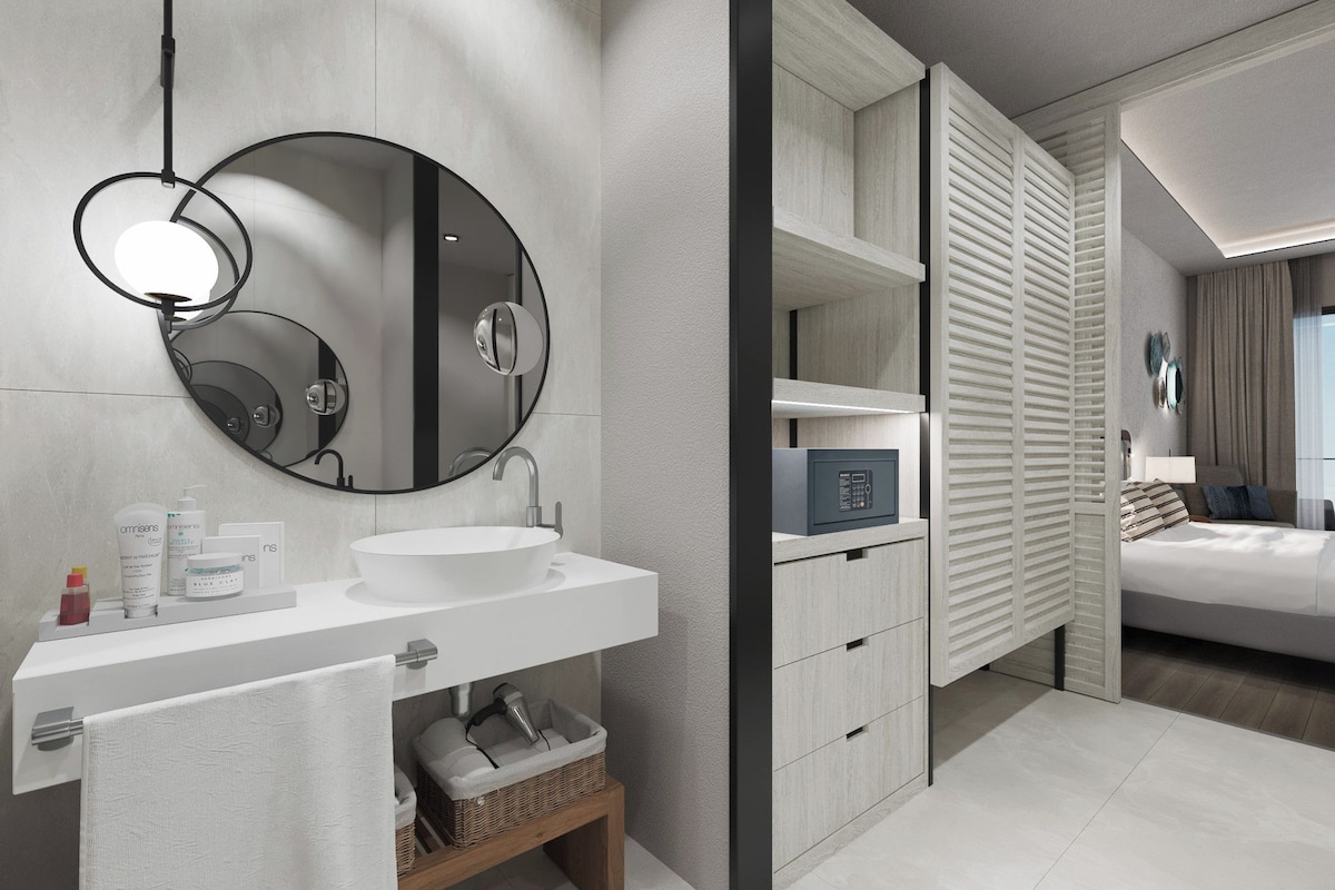 Un baño moderno con un espejo redondo, lavamanos blanco y un perchero para toallas.