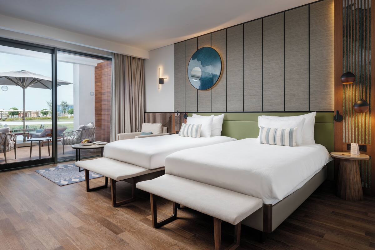 A hotel room with two beds, a large window, and a view of the outdoors.