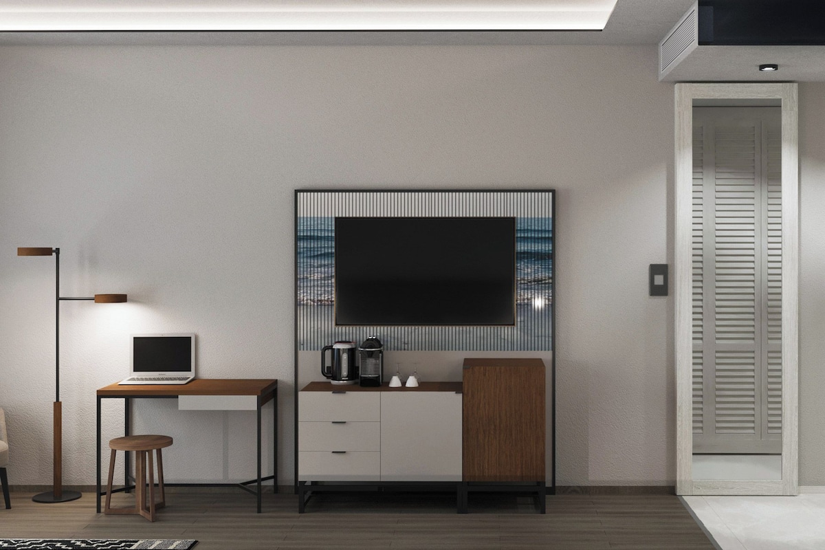 Una habitación moderna con escritorio, silla y un televisor de pantalla plana grande montado en la pared con vistas al mar.