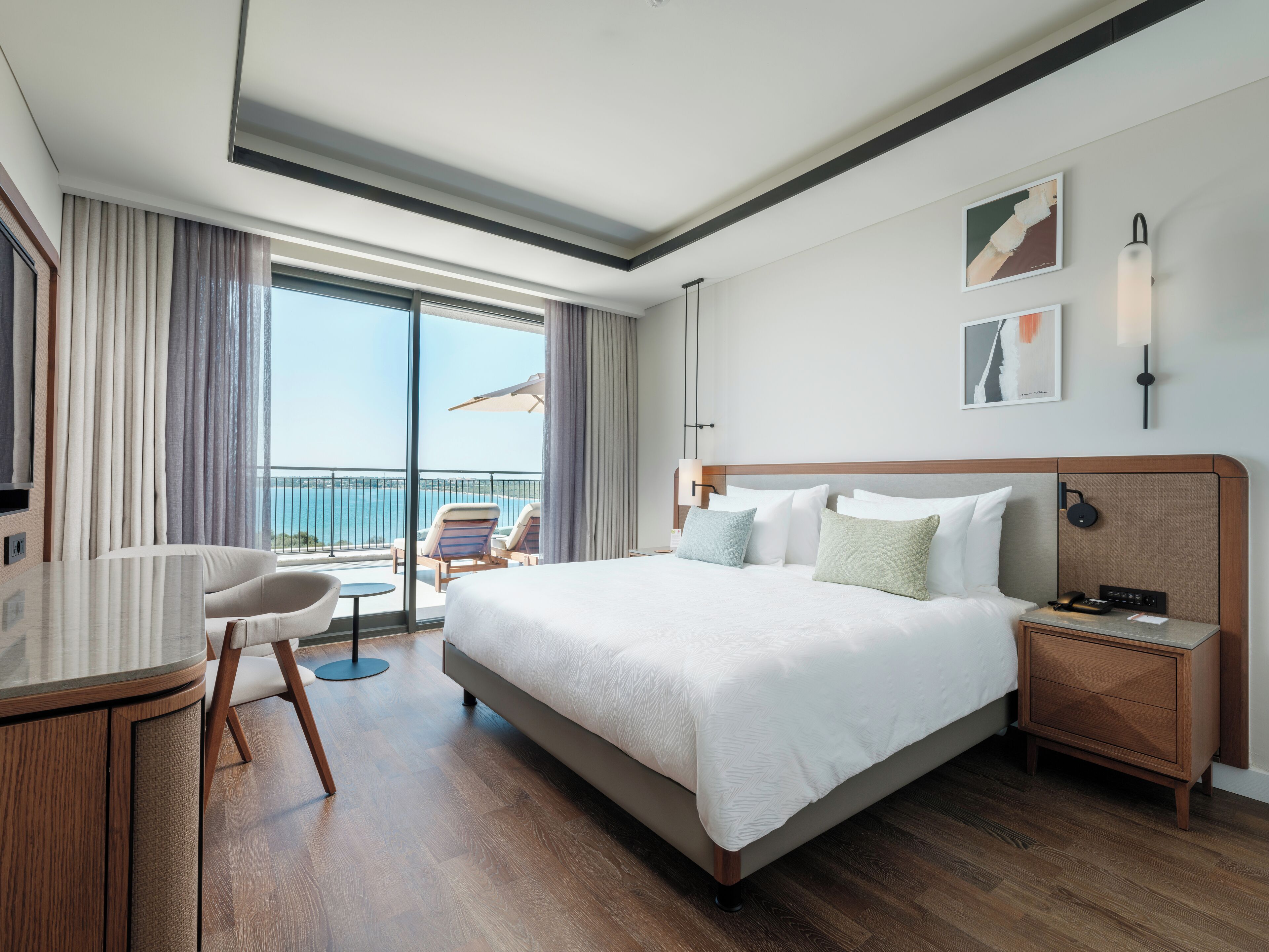 A hotel room with a large bed, a desk, a chair, and a view of the sea.
