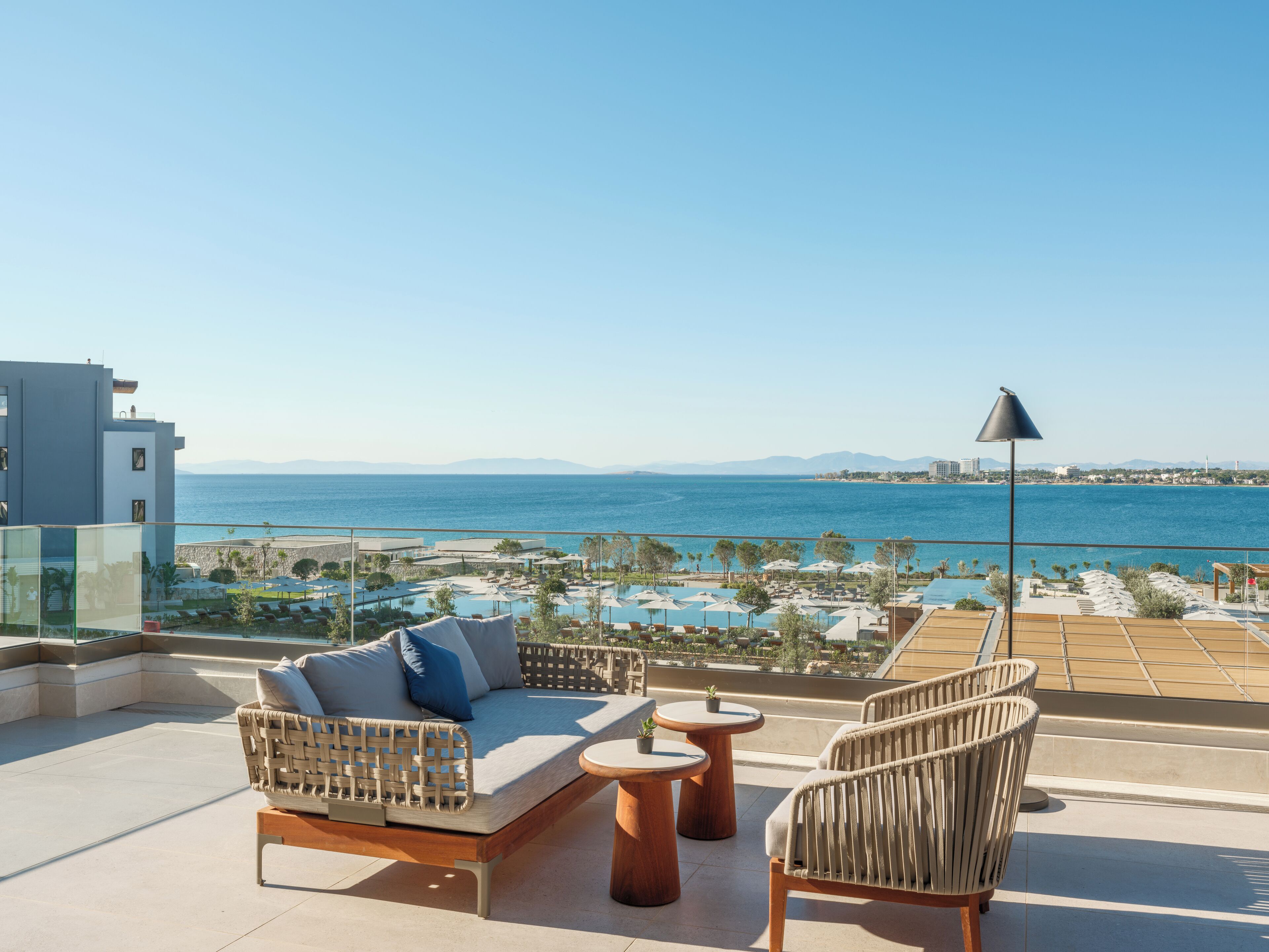 A rooftop terrace with a sofa, chairs, and a small table, overlooking a pool and the sea.