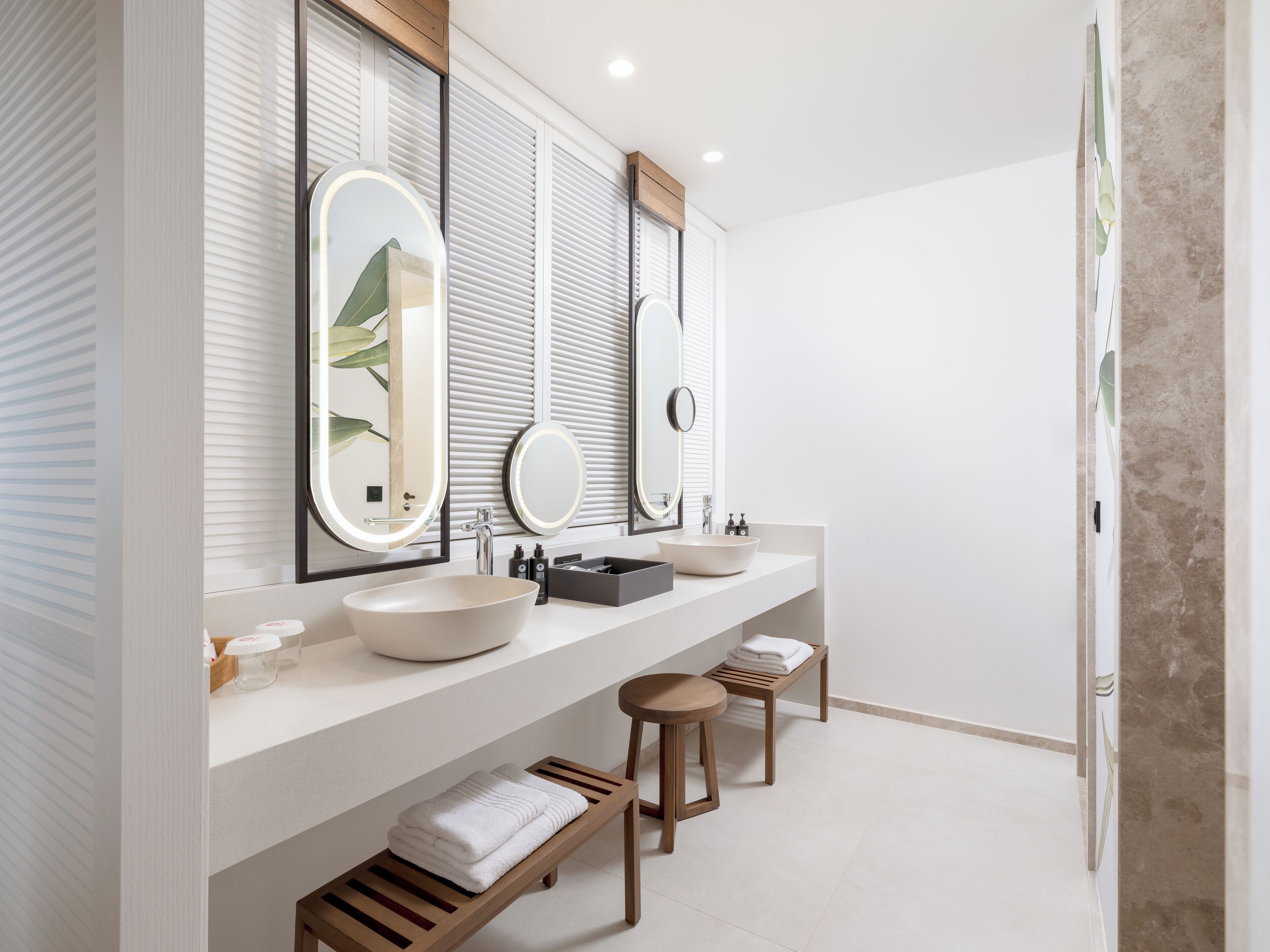 Une salle de bain moderne avec deux lavabos, de grands miroirs et un banc en bois.