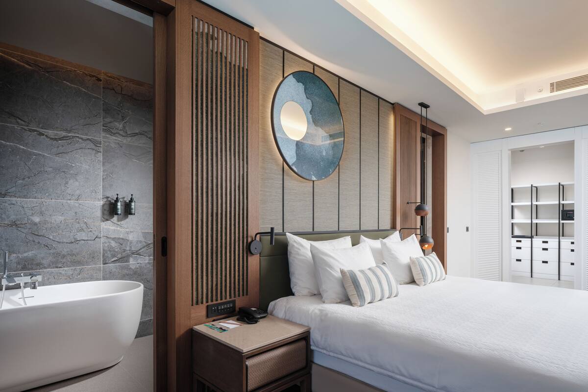A modern hotel room with a large bed, a built-in bathtub, and a wooden panel wall.