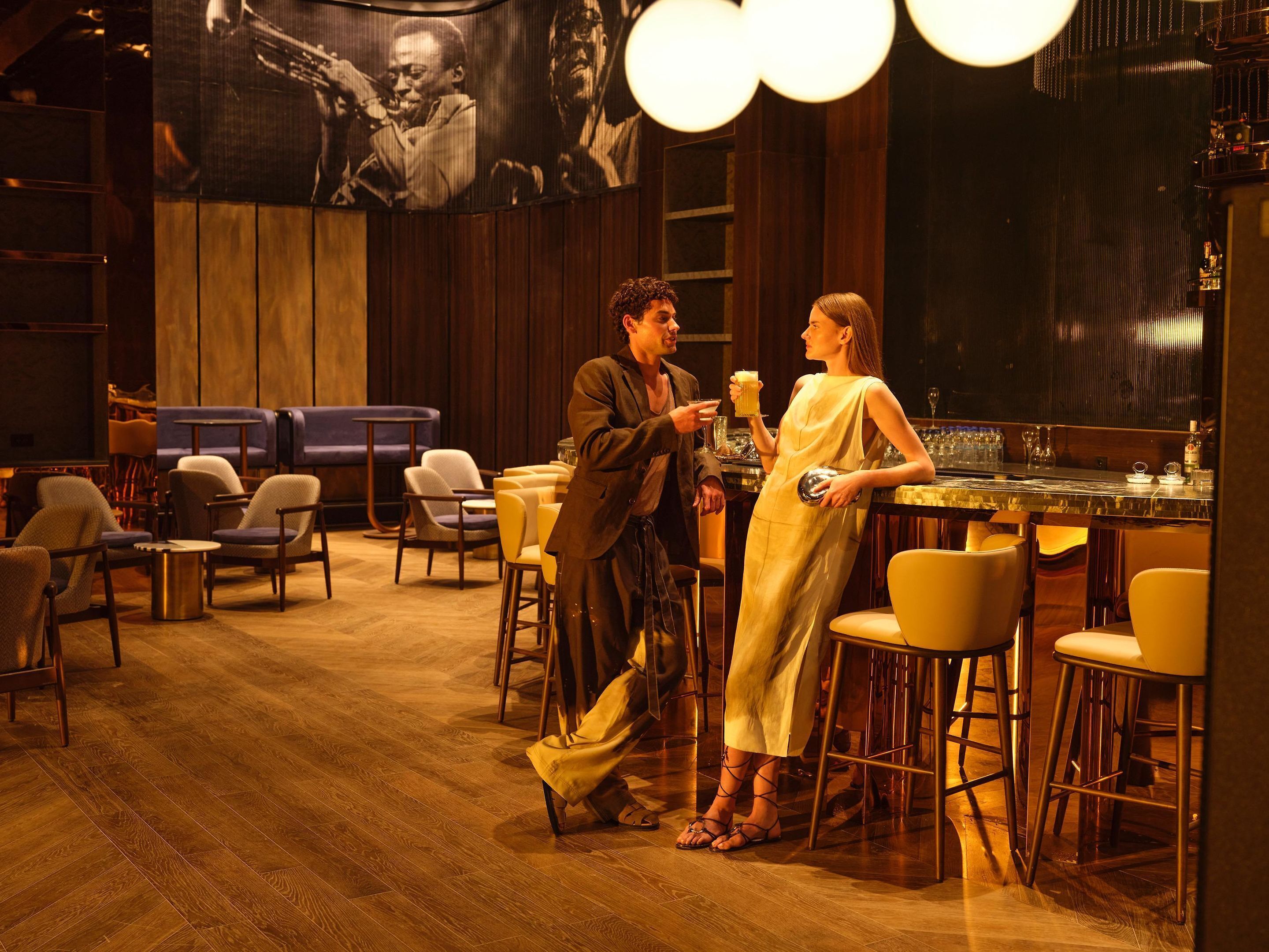 Zona de bar con suelo de madera, taburetes y una pantalla grande que muestra una película.