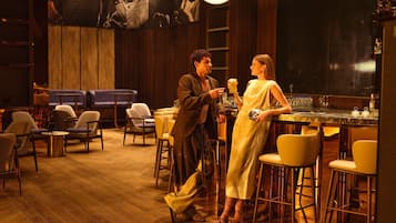 Zona de bar con suelo de madera, taburetes y una pantalla grande que muestra una película.