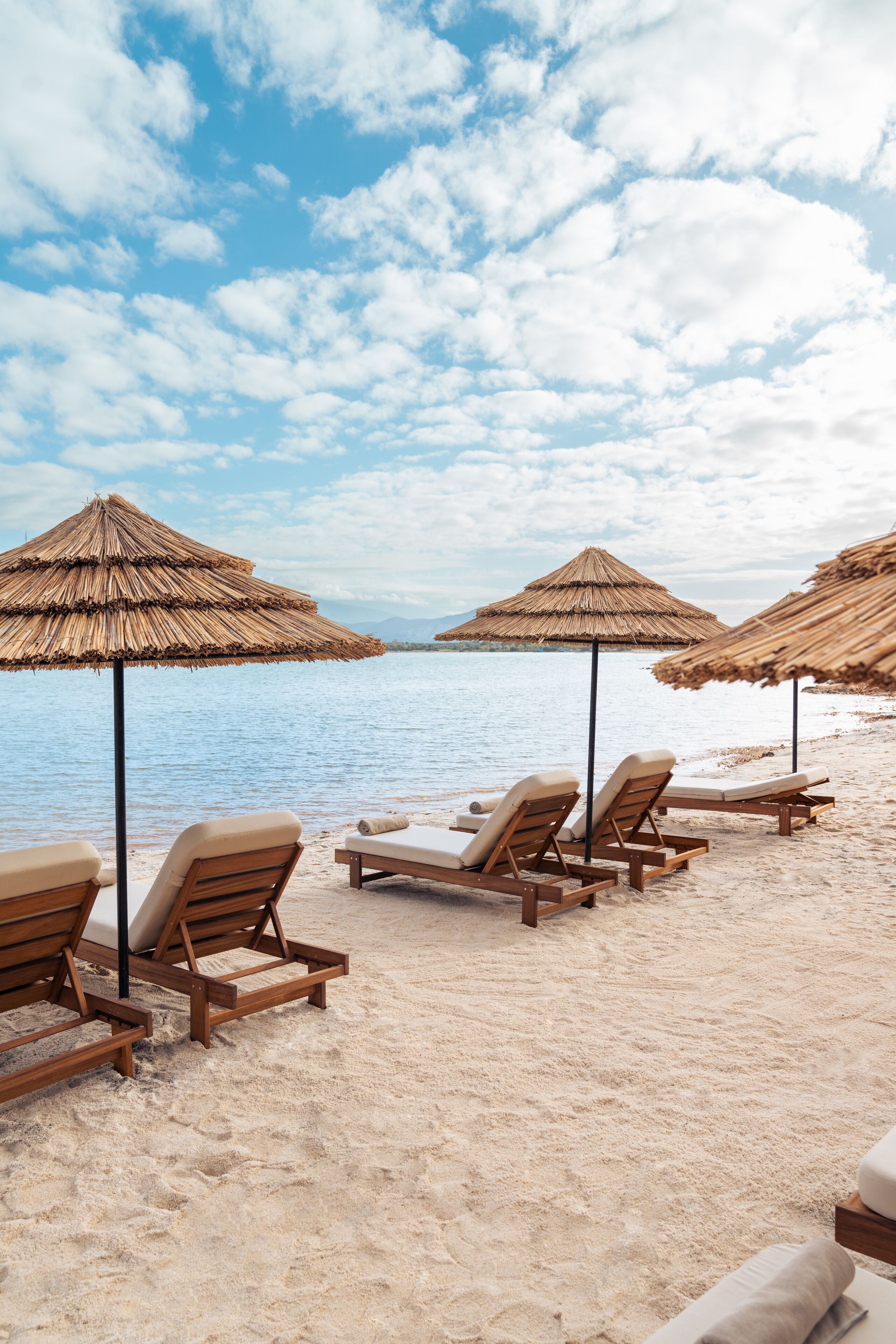 A beach with wooden lounge chairs and thatched umbrellas.