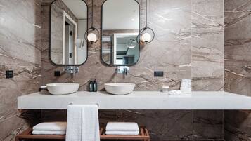 A modern bathroom with two sinks, a large mirror, and a wooden bench with towels.