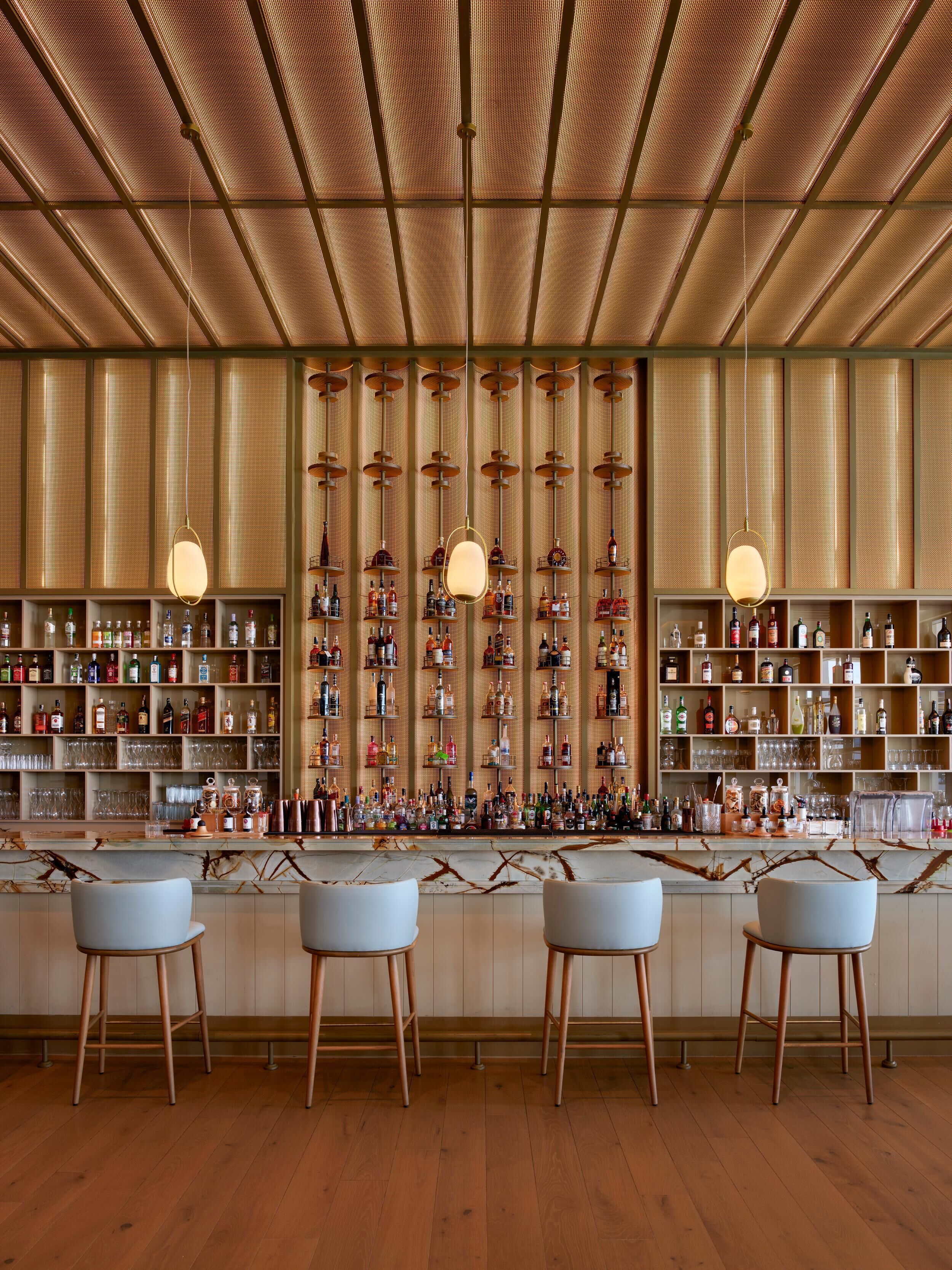 A bar with wooden floors, bar stools, and shelves stocked with bottles and glasses.