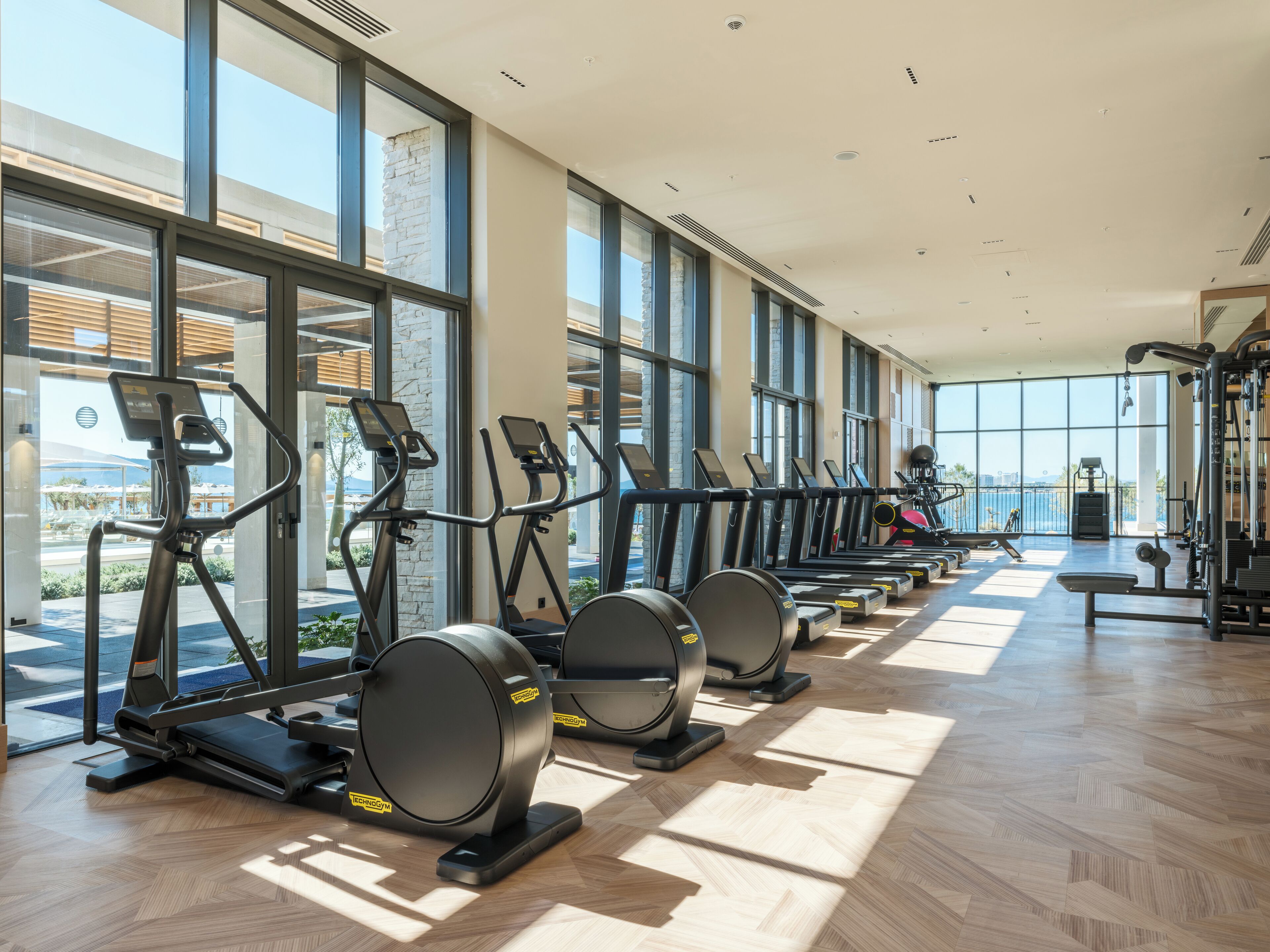 A gym with treadmills and exercise equipment, large windows, and a view of the outdoors.
