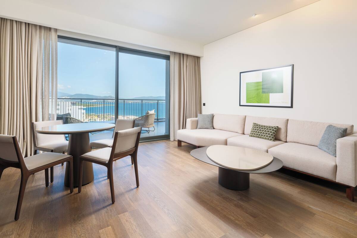 A modern living room with a sofa, chairs, a coffee table, and a balcony with a view of the sea.