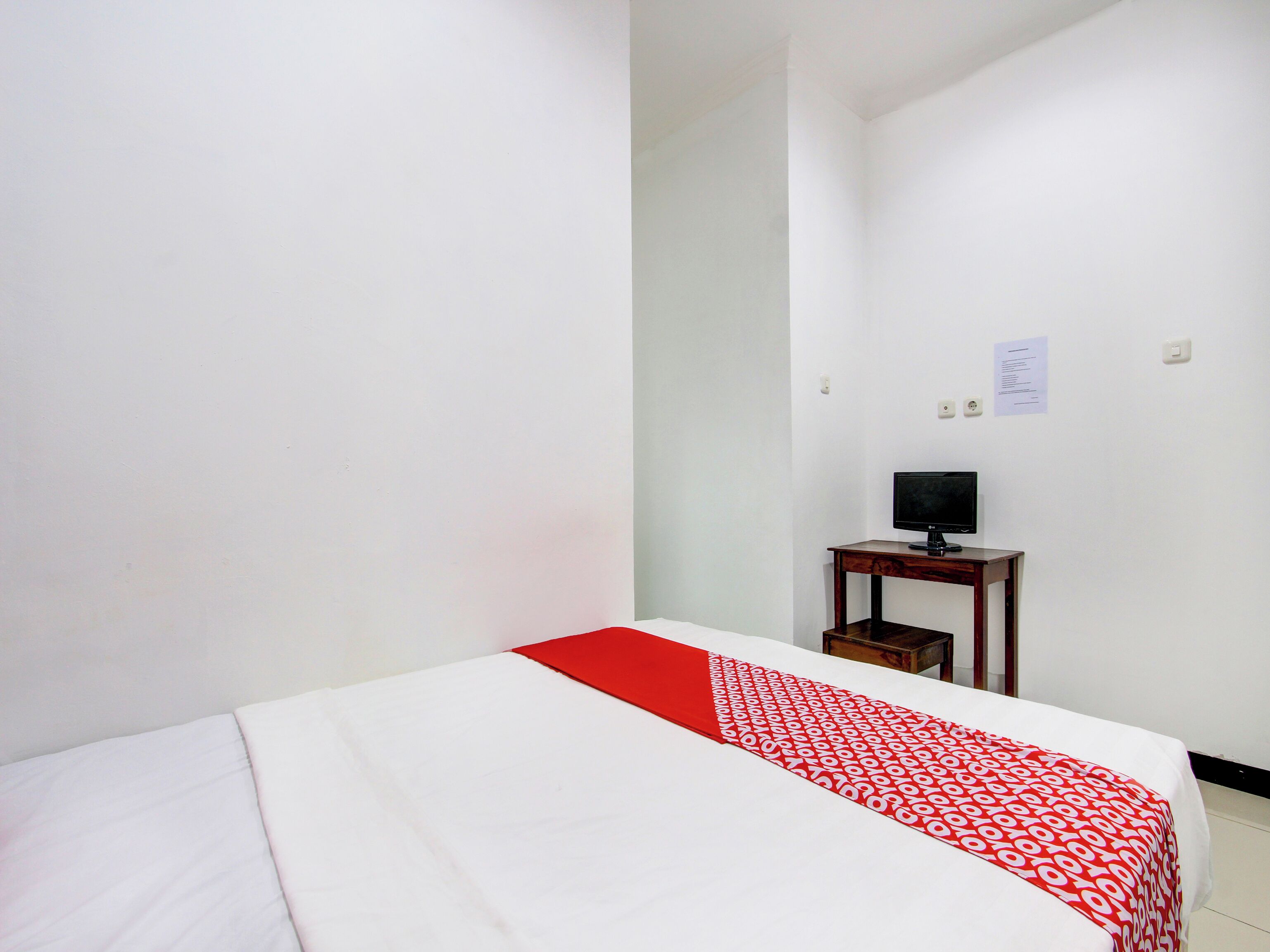 Una habitación de hotel con una cama, una mesita con televisor y una pared blanca con un aviso.