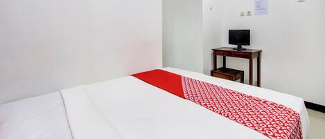 Una habitación de hotel con una cama, una mesita con televisor y una pared blanca con un aviso.