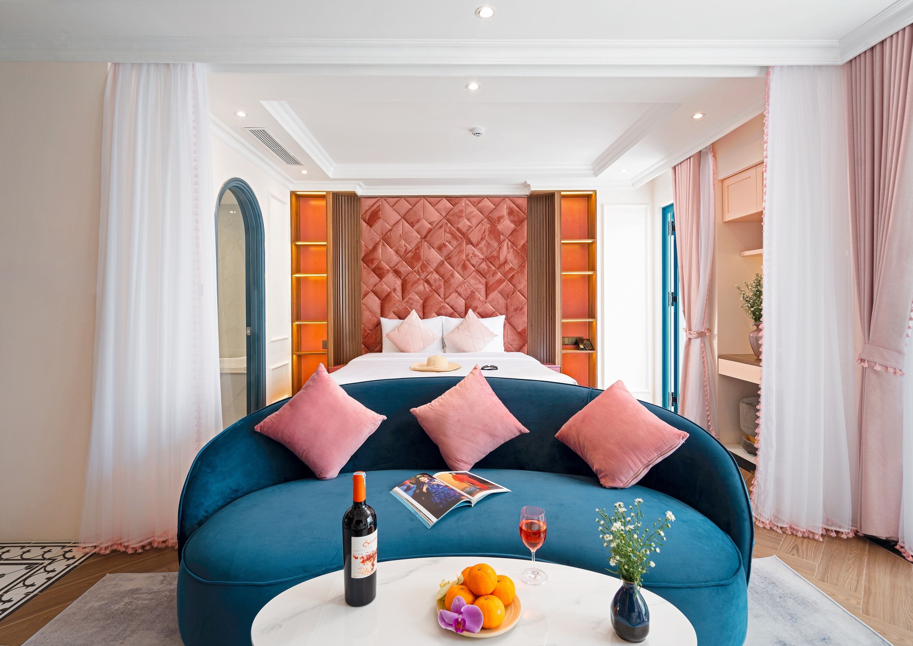 Une chambre avec un grand lit, un canapé bleu, une bouteille de vin et un verre de vin posés sur une table.